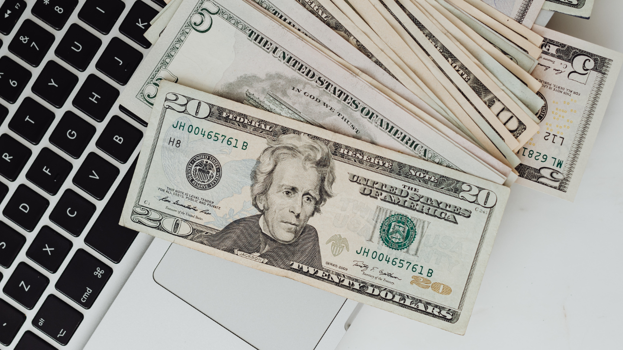Stack of $5, $10, and $20 bills splayed out over a laptop keyboard. 
